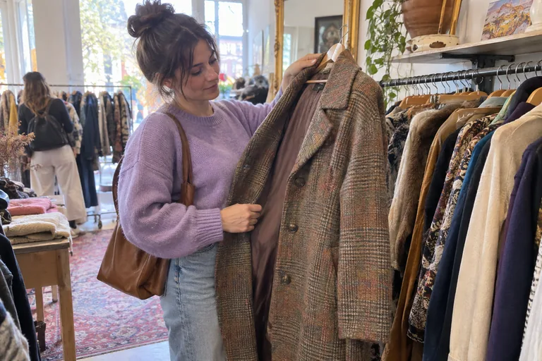 Une femme examine un manteau en laine vintage dans une friperie lumineuse