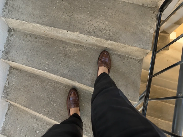 Une chaussure marron et un pantalon noir vus au niveau de l’ourlet