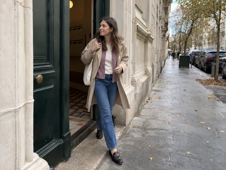 Une femme porte un trench léger, un cardigan mauve et un jean dans une rue à la mi-saison