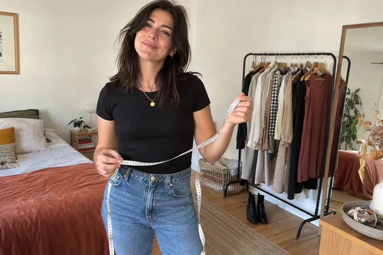 Une femme souriante tient un mètre ruban de couturière dans une chambre lumineuse