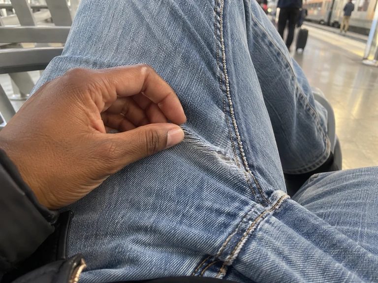 Une main examine une couture usée sur un jean