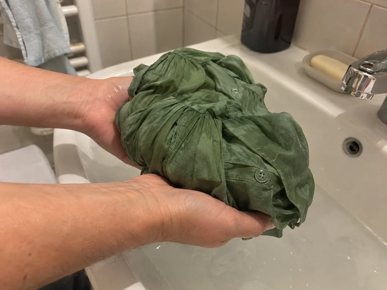 Des mains soutiennent une blouse mouillée au-dessus d’une bassine