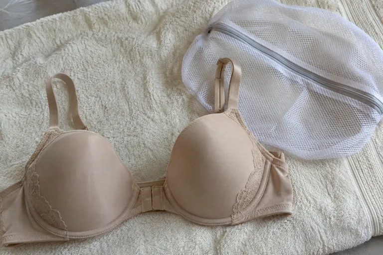Un soutien-gorge beige posé sur une serviette blanche à côté d’un filet de lavage