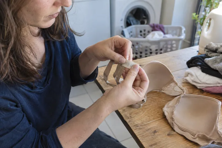 Une femme examine une petite étiquette sur un soutien-gorge beige près d’un panier à linge