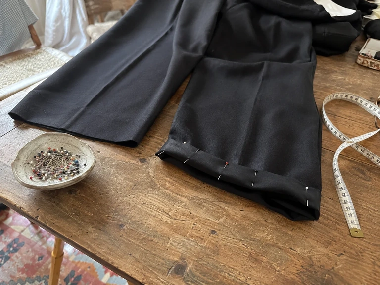 Des épingles maintiennent un ourlet provisoire sur un pantalon à plat