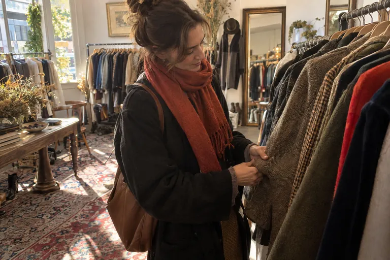 Une femme examine la matière d’un manteau en laine dans une friperie lumineuse