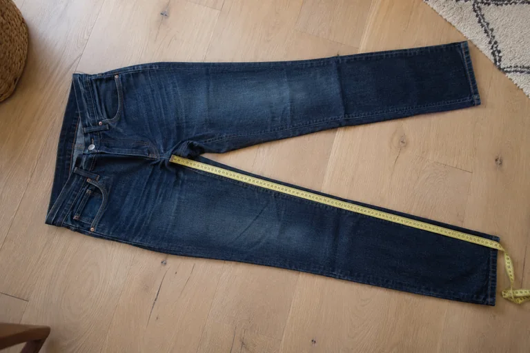Un jean bleu posé à plat avec un mètre ruban le long de la couture intérieure d’une jambe
