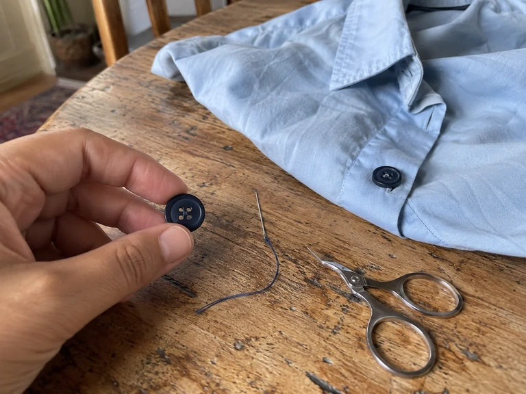 Un bouton et une aiguille attendent à côté d’une chemise