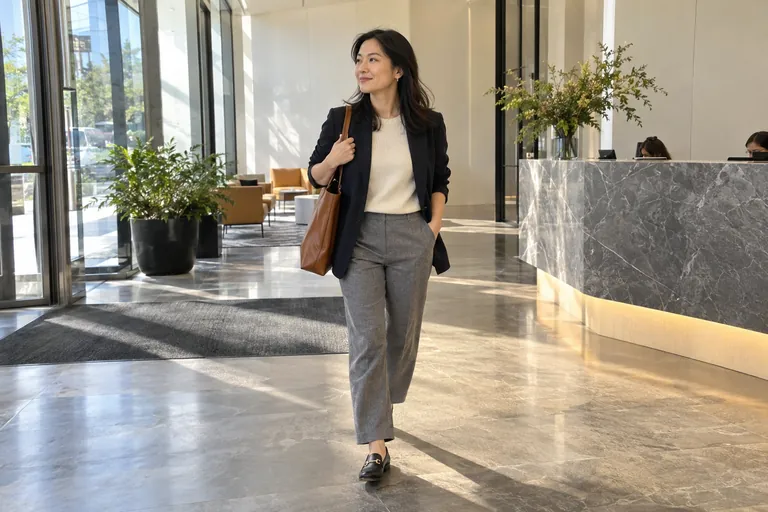 Une femme en blazer marine et pantalon gris entre dans un hall de bureau lumineux