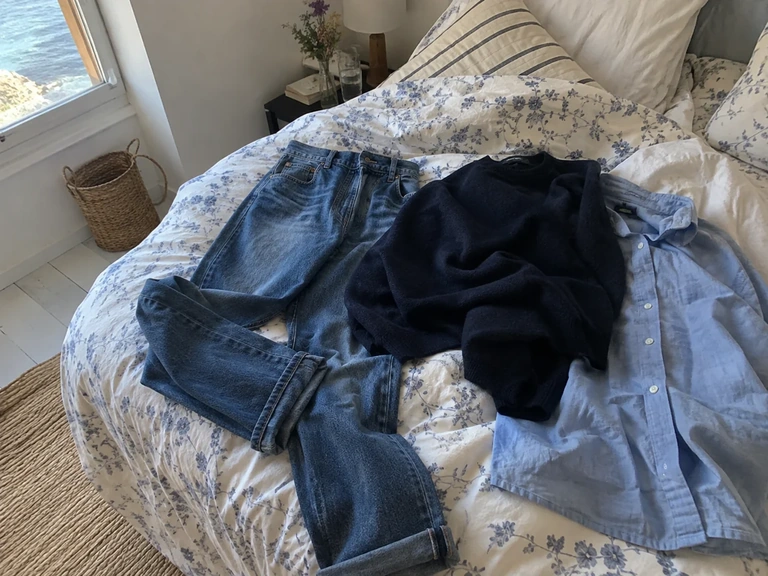Trois vêtements bleus de textures différentes sont posés sur un lit