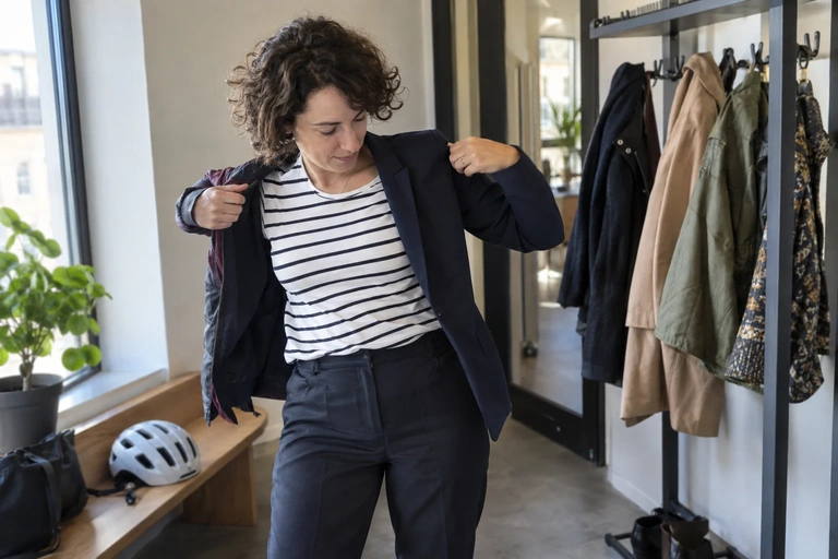 Une femme enfile une veste dans l’espace vestiaire du bureau