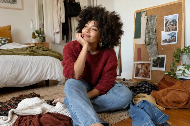 Une jeune femme assise au sol entourée de ses vêtements préférés et d’un tableau d’inspiration